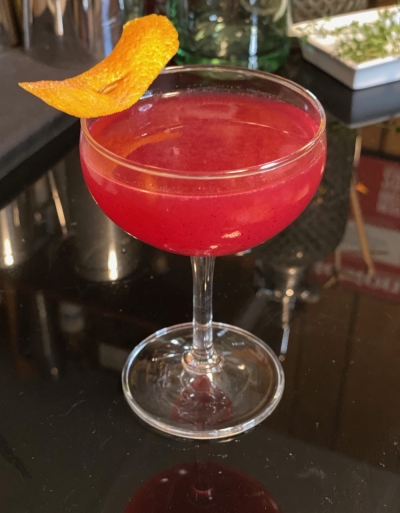 Coupe cocktail glass with bright berry-colored liquid and orange peel