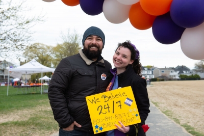 Two Walk participants smile under ballon arch with sign that says: We Believe 24-7